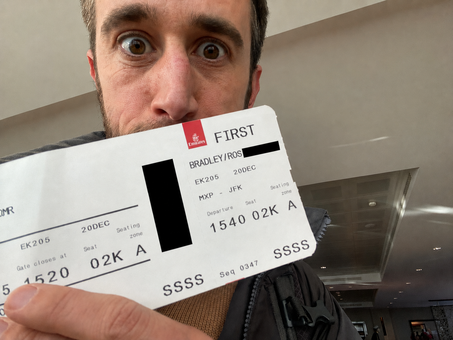 Ross Bradley holding his Emirates First Class boarding pass at the Milan airport
